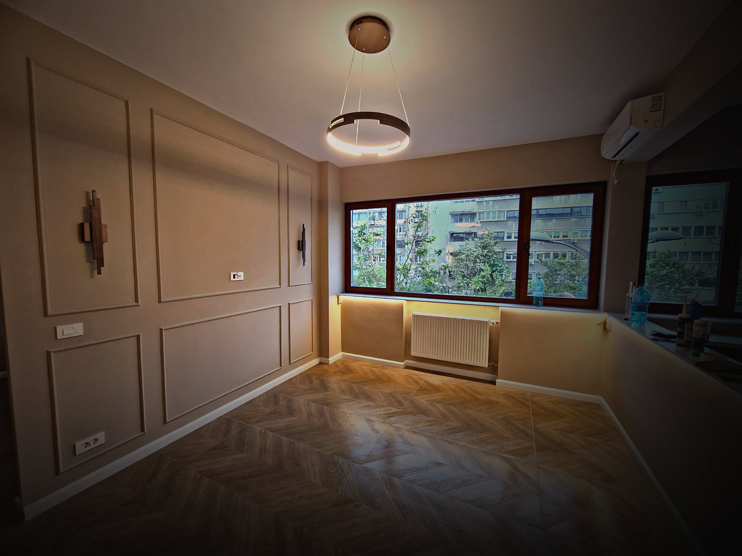 Același living după renovare: boiserie, parchet în spic, iluminat ambiental și pendul inelar.